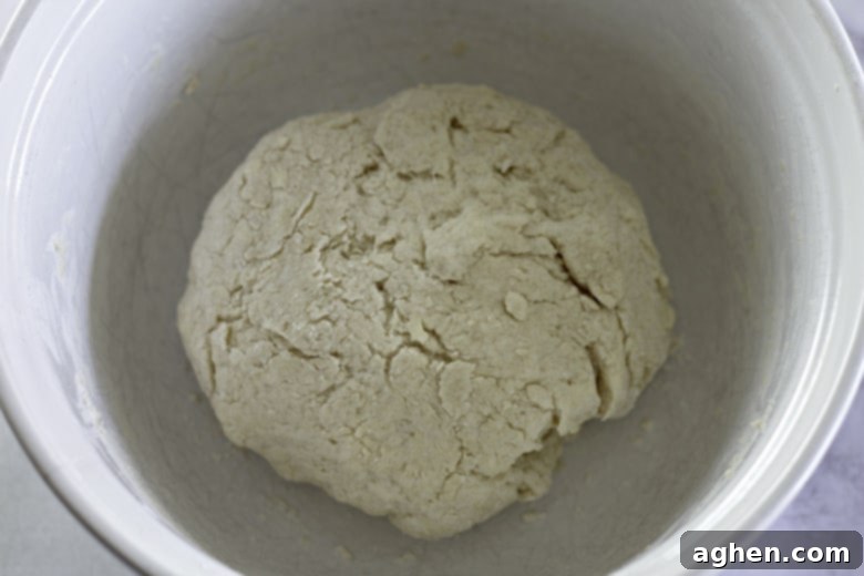 Cold buttermilk being added to the flour and butter mixture in a bowl, with a spatula gently stirring to form a soft biscuit dough.
