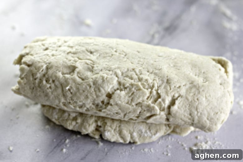 A pair of hands demonstrating the letter fold technique on biscuit dough, folding one third over the middle to create layers.