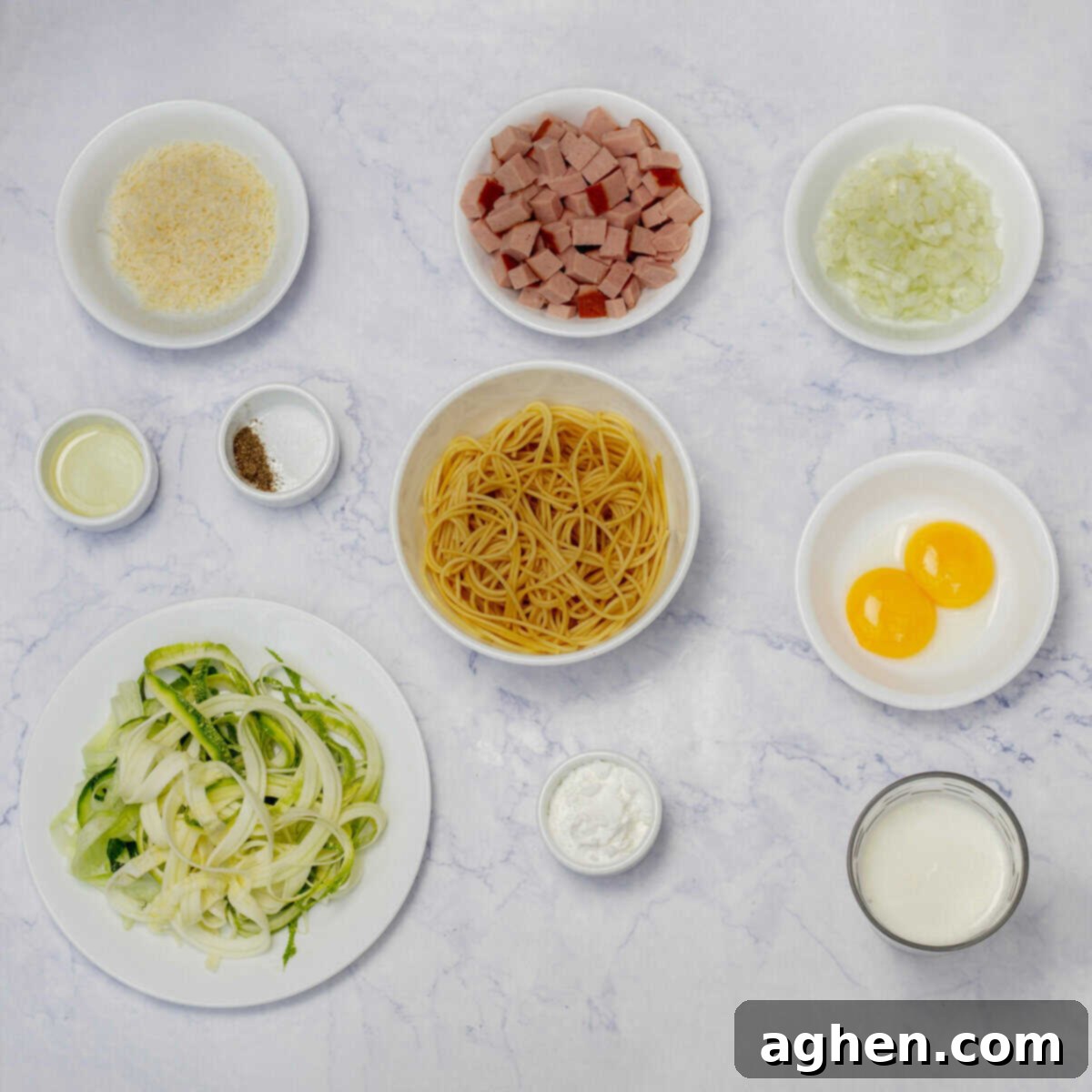 Light carbonara ingredients including whole-wheat pasta, spiralized zucchini, chopped onion, egg yolk, cornstarch, fresh parmesan, and diced smoked turkey ham in separate dishes.