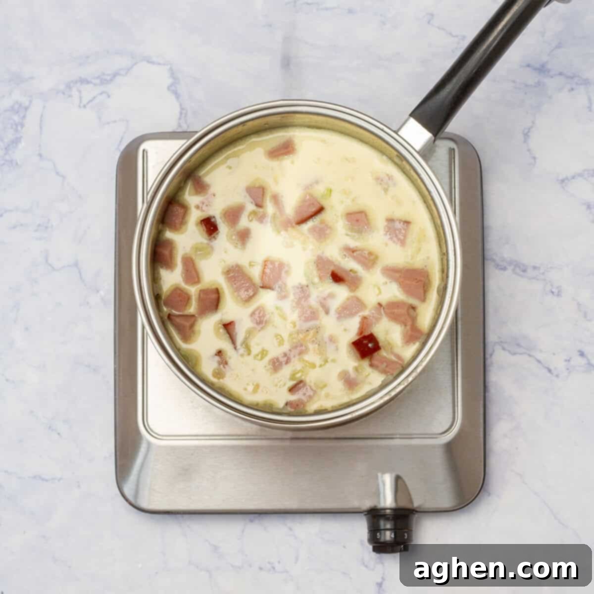 Creamy sauce mixture being poured over the browned turkey ham and onions in a pan, stirred gently.