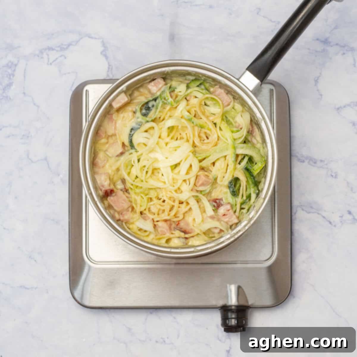 All the sauce ingredients in a pan combined with cooked pasta and spiralized zucchini, tossed together.