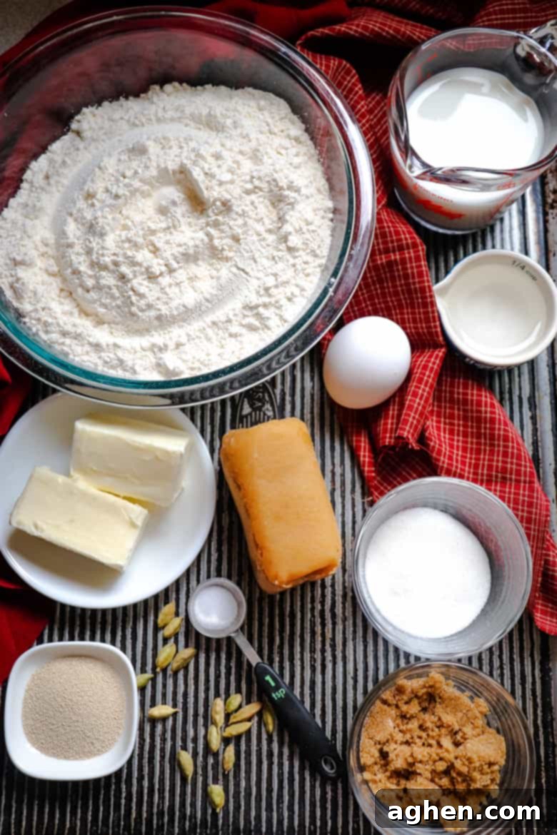 A selection of dough ingredients: flour, butter, egg, milk, sugar, almond paste, and yeast, neatly arranged on a counter.