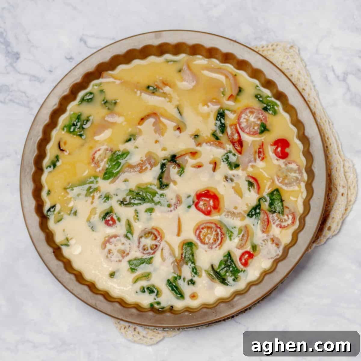 Whisked egg mixture and cooked vegetables in a pie pan, ready to be baked into a frittata.