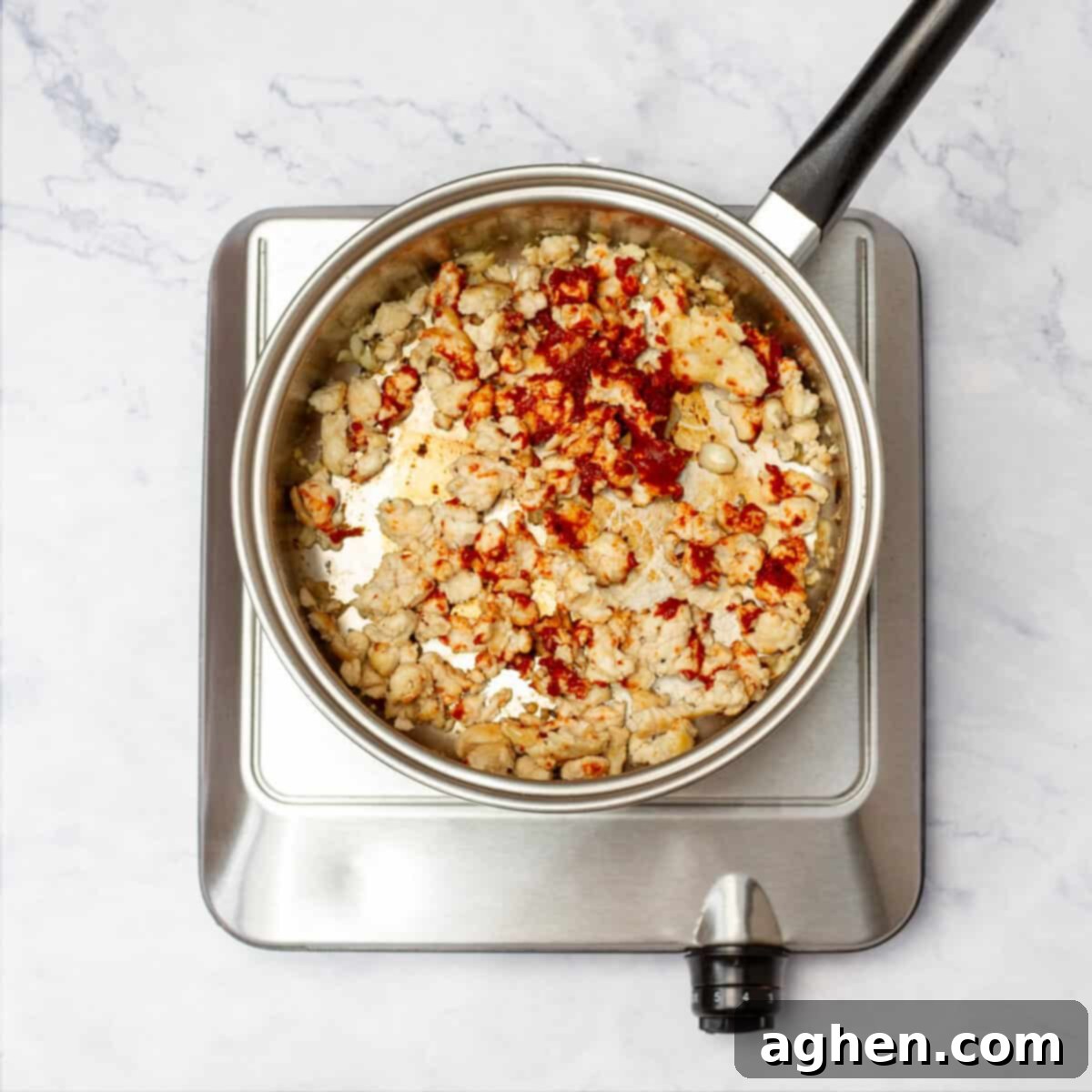 Seasoned ground turkey cooking in a non-stick pan on a stovetop, with a spoon breaking up the meat.