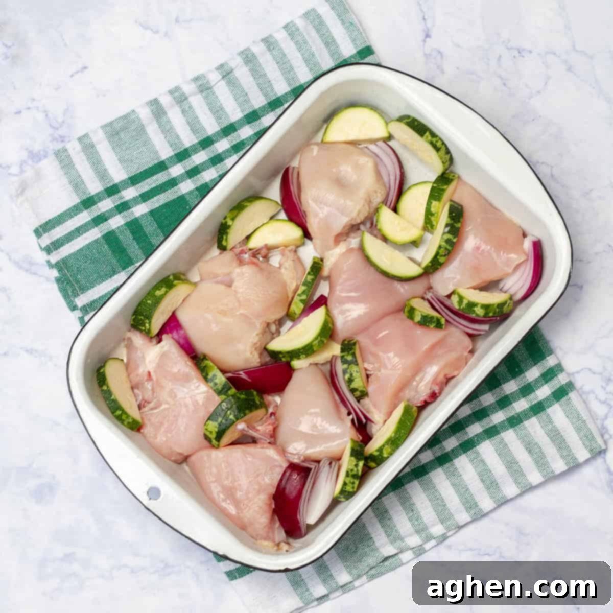Yunan Limonlu Tavuk: Diyette Olanlar İçin İdeal Yaz Akşamı 4 Raw chicken pieces sitting atop sliced zucchini and garlic in a baking dish.