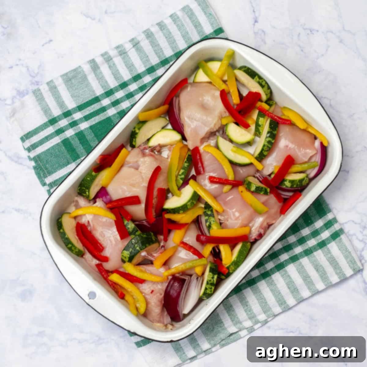 Yunan Limonlu Tavuk: Diyette Olanlar İçin İdeal Yaz Akşamı 5 Raw chicken pieces sitting atop sliced zucchini and garlic with sliced red bell peppers on top in a baking dish.
