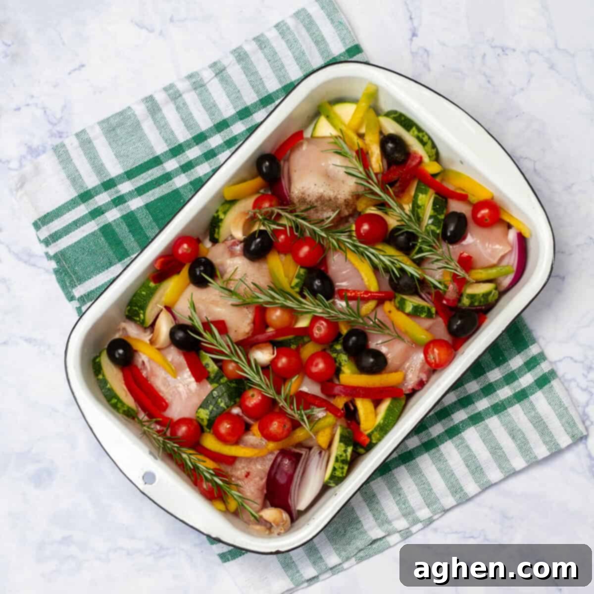 Yunan Limonlu Tavuk: Diyette Olanlar İçin İdeal Yaz Akşamı 6 Raw chicken pieces sitting atop sliced zucchini and garlic with sliced red bell peppers and black ilives on top in a baking dish.