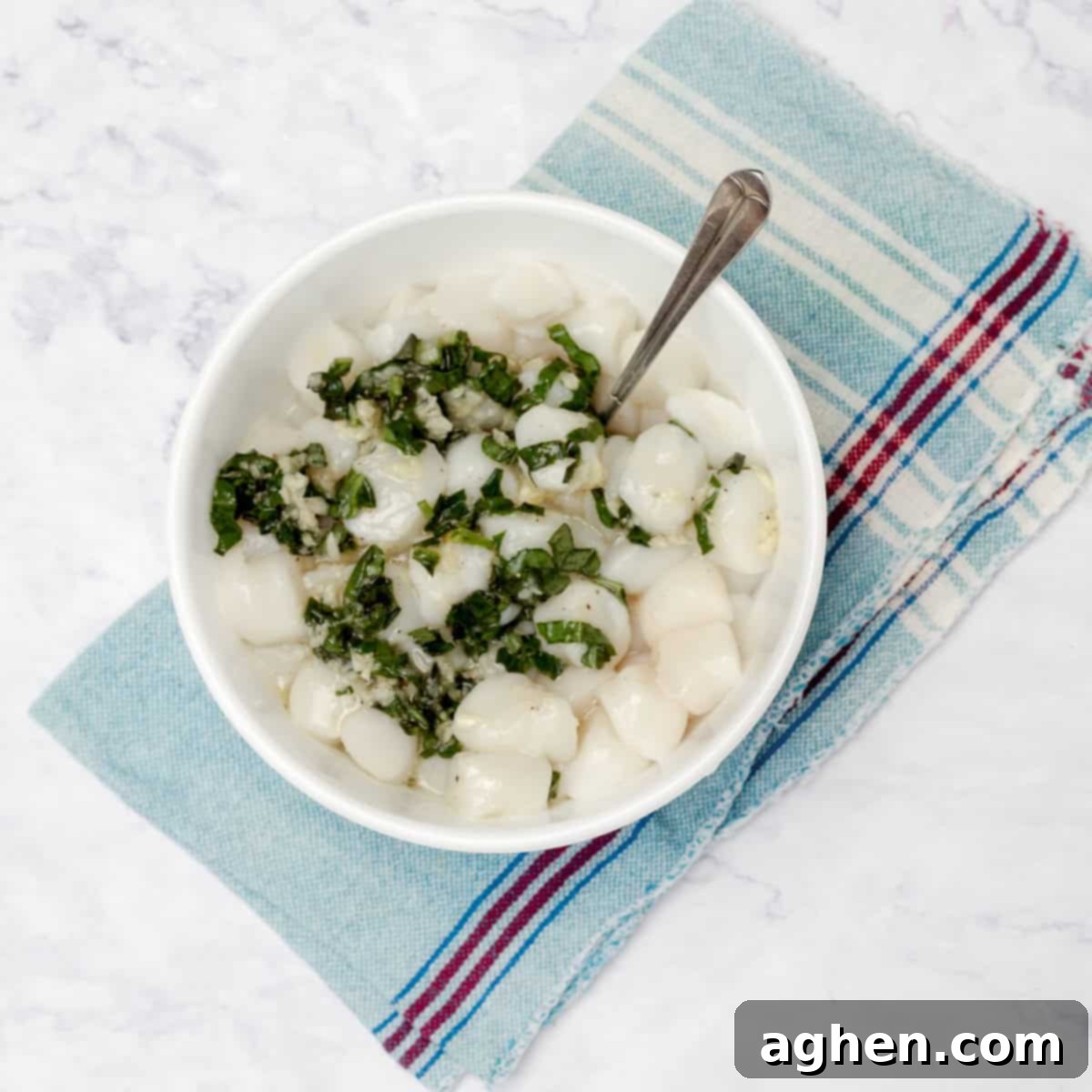 Raw scallops marinating in a bowl with garlic, basil, salt, and pepper.