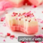 Piece of Valentines fudge with pink and white layers and topped with festive pink and red sprinkles. A bite has been taken out of the fudge.