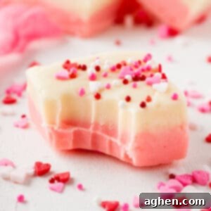 Piece of Valentines fudge with pink and white layers and topped with festive pink and red sprinkles. A bite has been taken out of the fudge.
