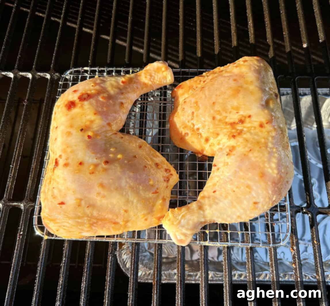 Raw, sauced chicken leg quarter smoking on an offset smoker grill.