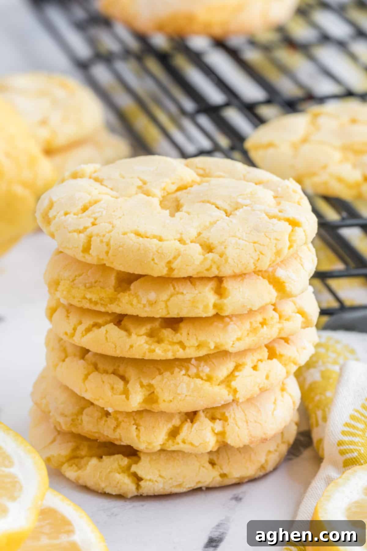 Stacked soft and chewy lemon cake mix cookies with more cookies cooling on a wire rack in the background.