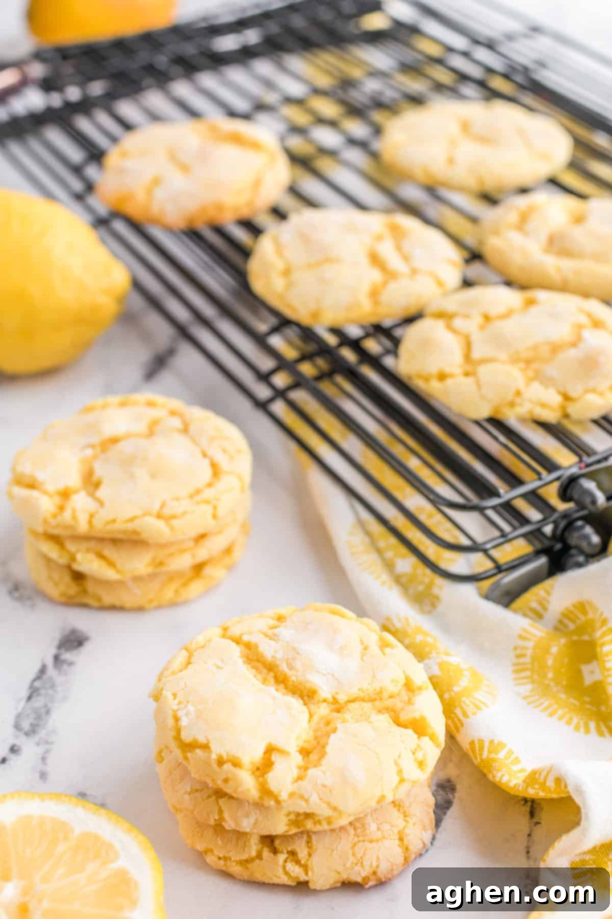 A stack of golden lemon cake mix cookies next to a wire cooling rack with more freshly baked cookies.