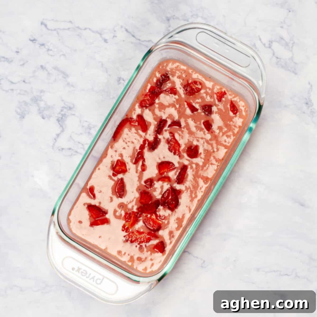 The velvety blended ice cream base is poured into an elegant glass dish, topped with fresh, vibrant strawberry slices, awaiting its time in the freezer to set.