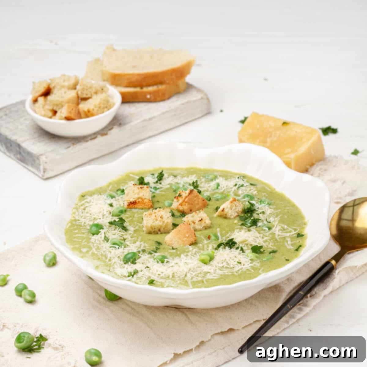 Creamy Pea and Spinach Soup in a bowl with croutons on top and a spoon on the side.