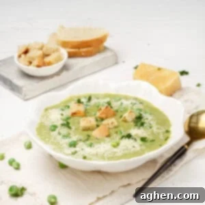 Creamy Pea and Spinach Soup in a bowl with croutons on top and a spoon on the side.