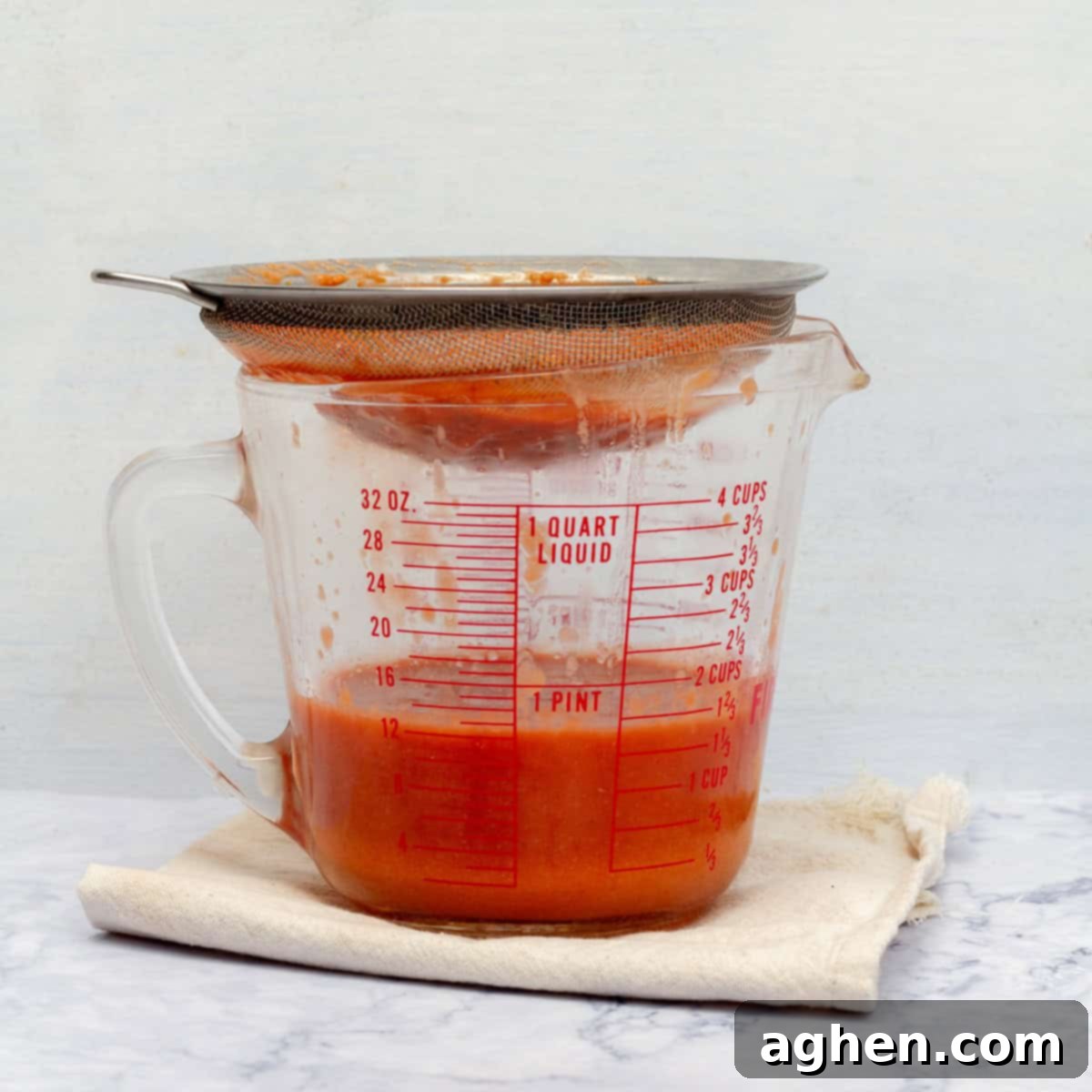 Blended soup being poured through a strainer into a measuring cup. 