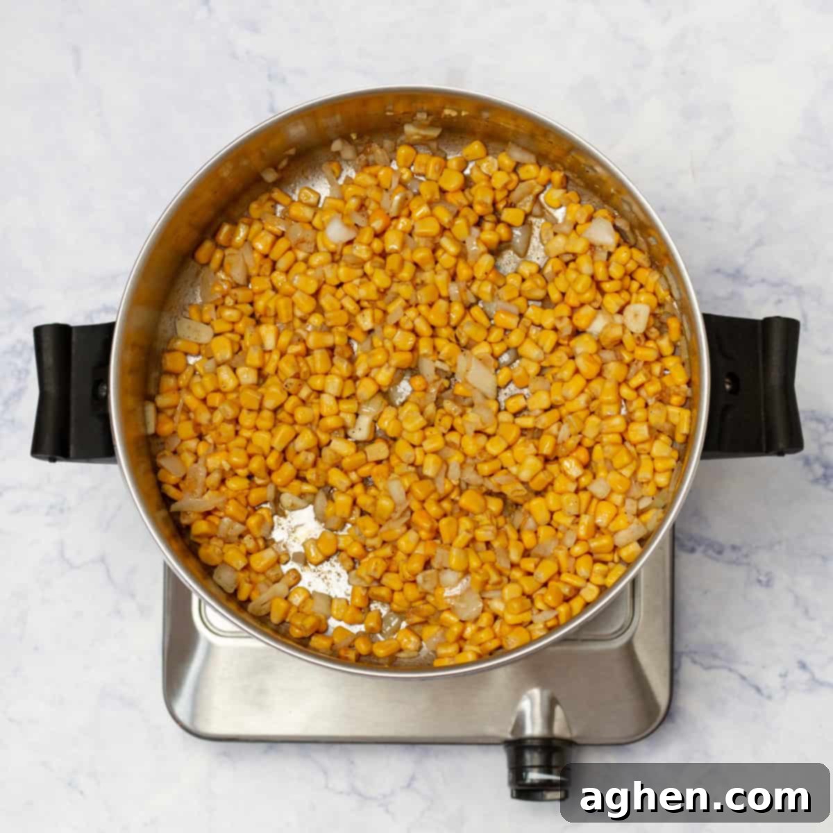 Sweet corn cooking in a pot with fragrant spices and onion, gaining a slight char that enhances its flavor profile.