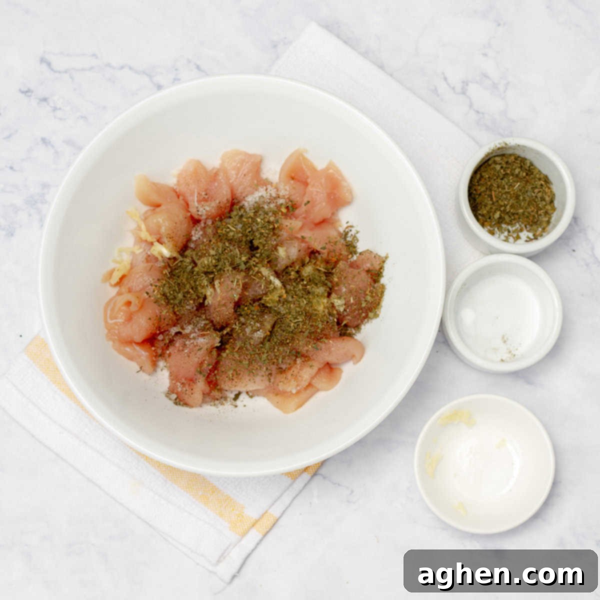 Cubed raw chicken breast marinating in a small bowl with spices, ready for cooking.
