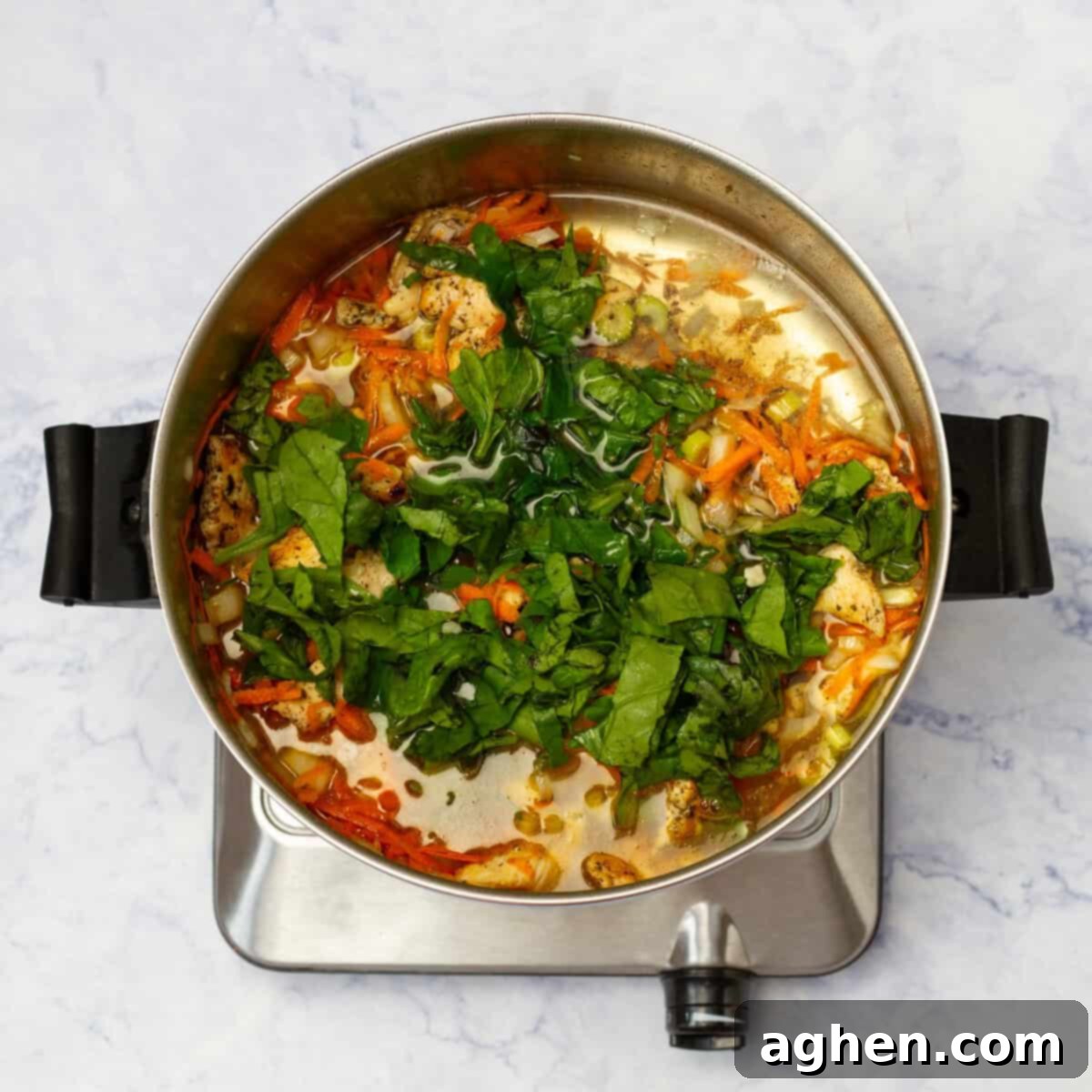 Cooked chicken breast and sautéed vegetables simmering in a pot with chicken broth, building flavor for the soup.