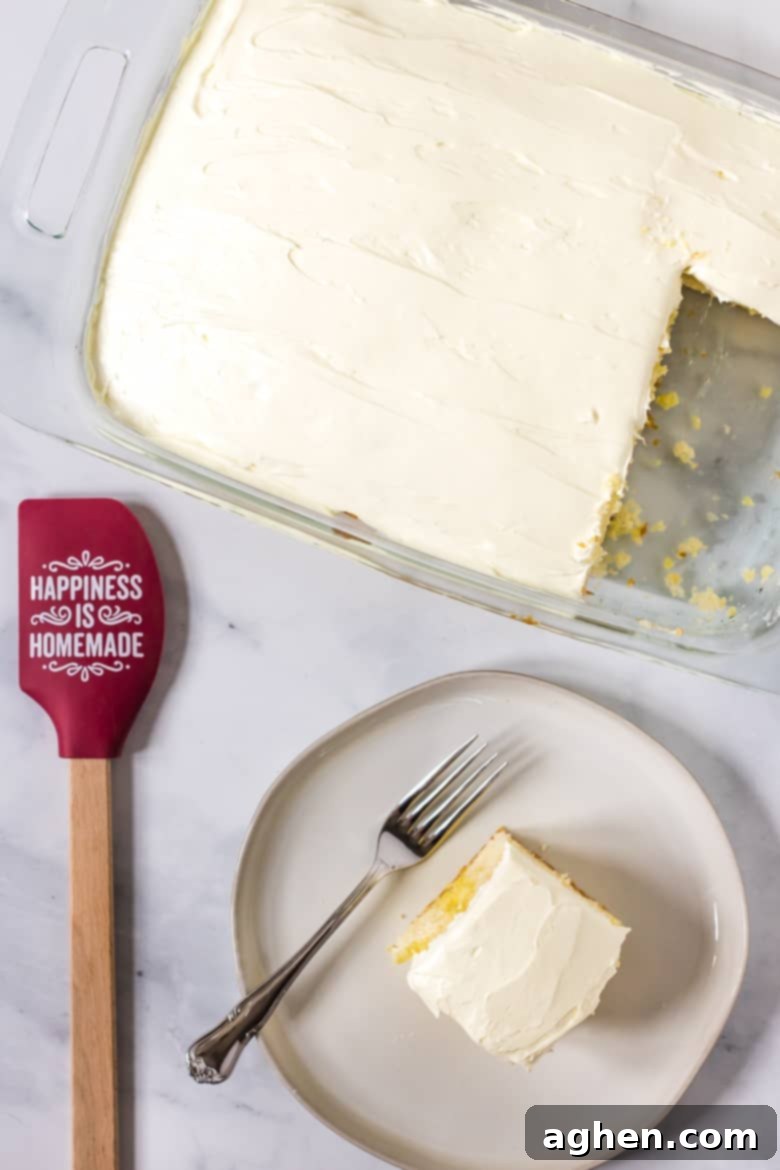 A single slice of lemon sheet cake with Jello, featuring visible Jello pockets and a creamy frosting, elegantly served on a white plate with a fork.