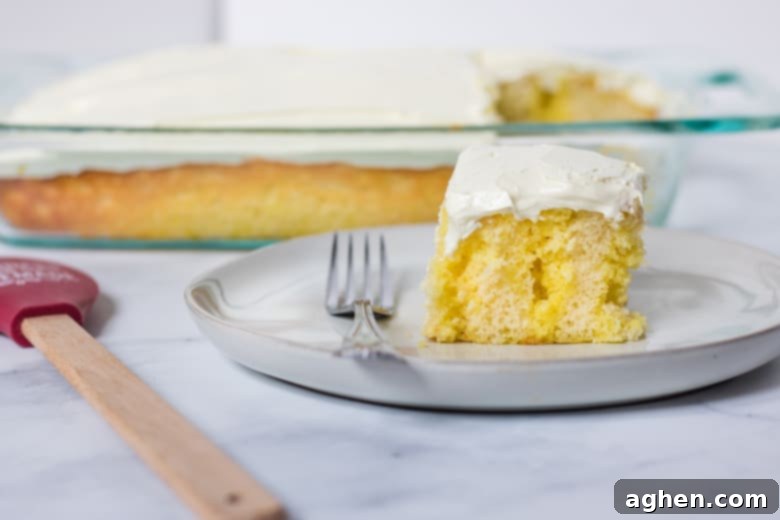 A freshly frosted lemon poke cake, topped with smooth, creamy lemon frosting and garnished with delicate lemon zest, cut into serving squares.