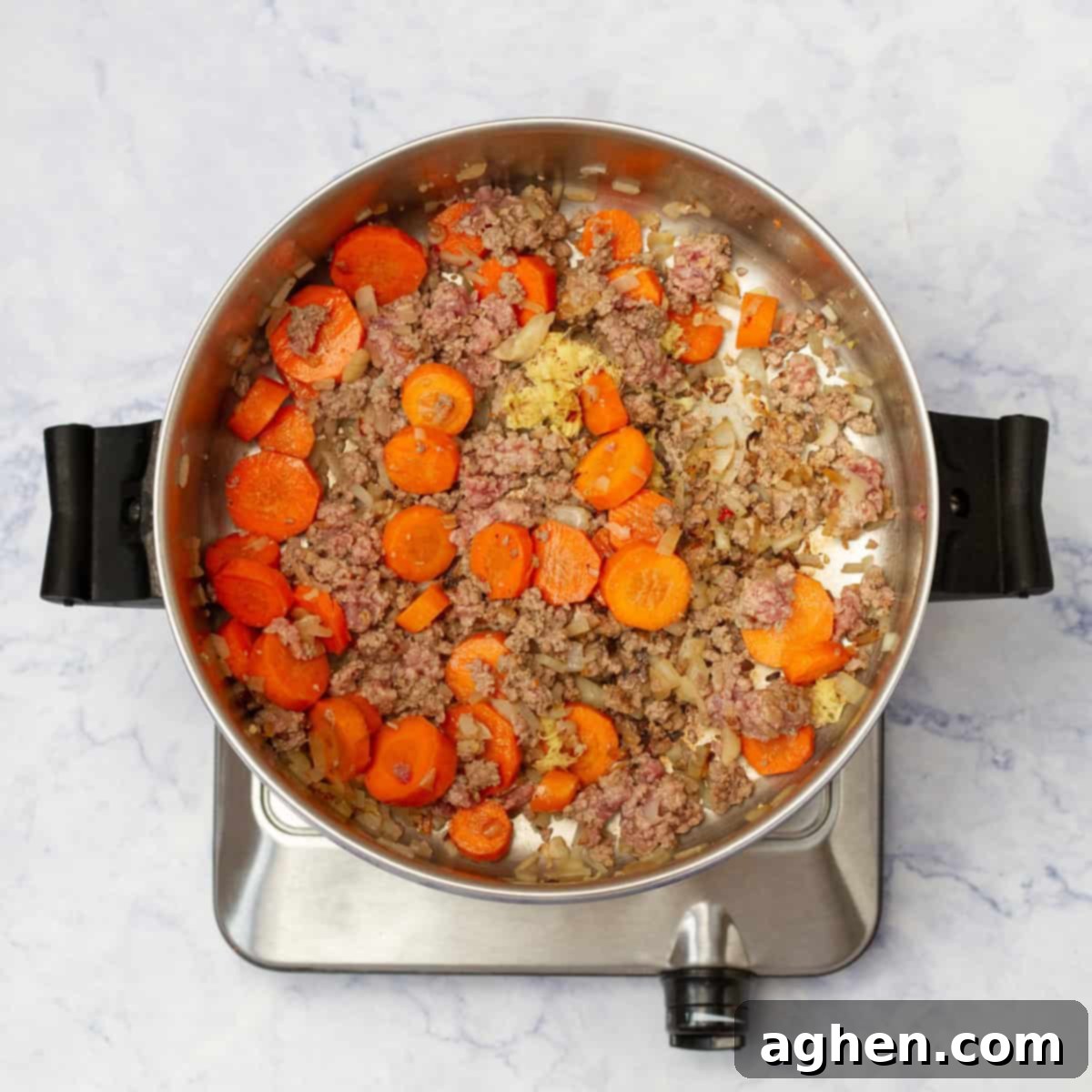 Aromatics like finely diced onions and minced garlic cooking in a large pan with sliced carrots, releasing their fragrant essence and softening as they sauté.