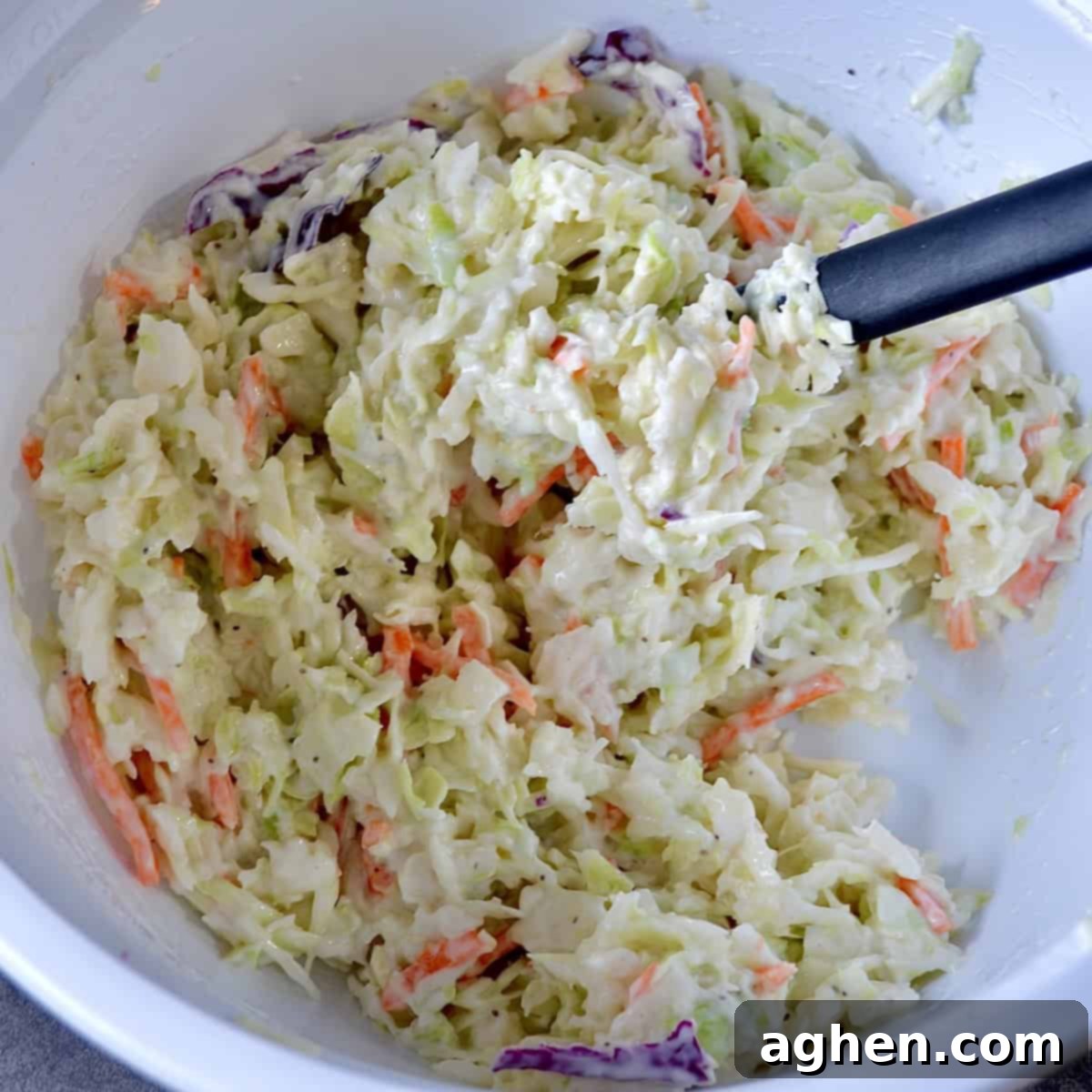 Skinny Creamy Coleslaw 5 Mixing the creamy coleslaw dressing into shredded cabbage and carrots in a large bowl