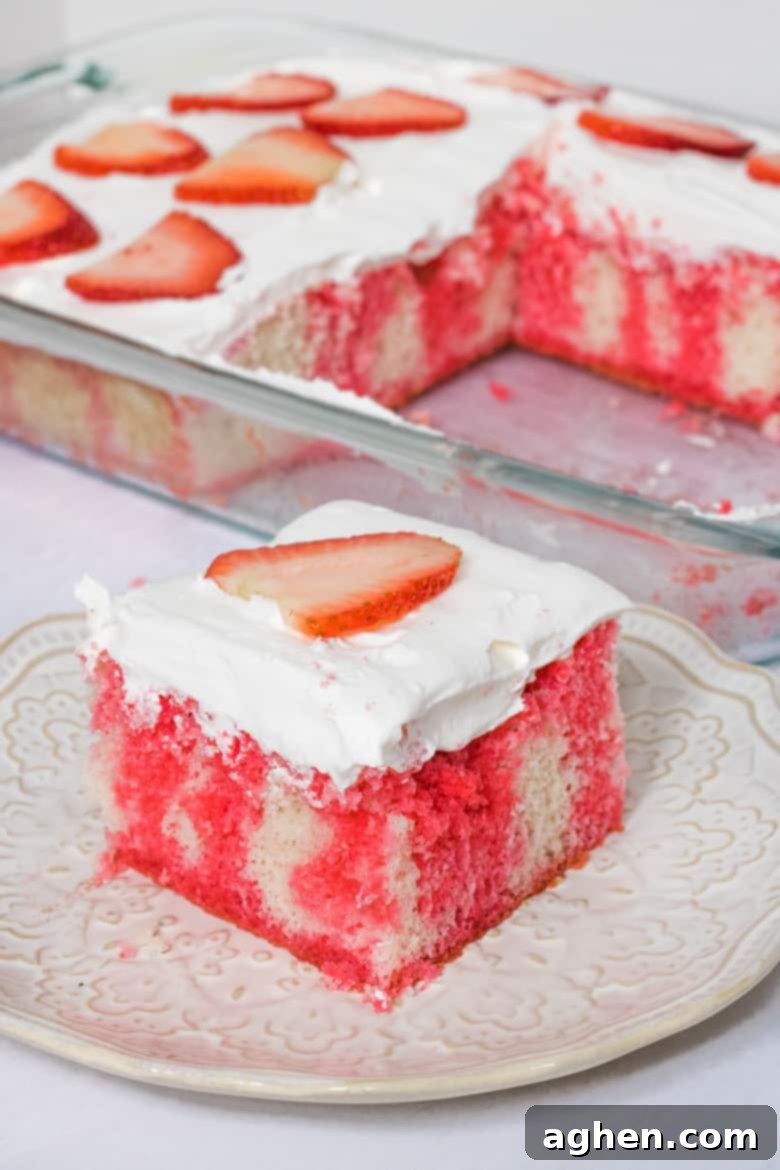 Strawberry jello poke cake made with vanilla cake, Cool whip frosting, and topped with fresh sliced berries.