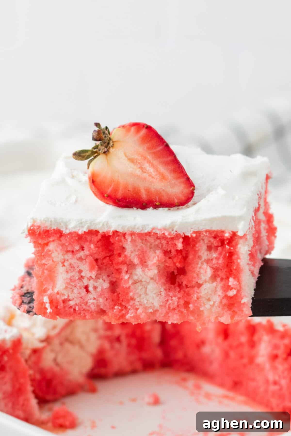 Spatula lifting slice of strawberry jello poke cake from cake dish.