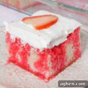 Square slice of strawberry jello poke cake made from white cake with red Jello drips through it. The cake is topped with cool whip topping and a slice of strawberry.