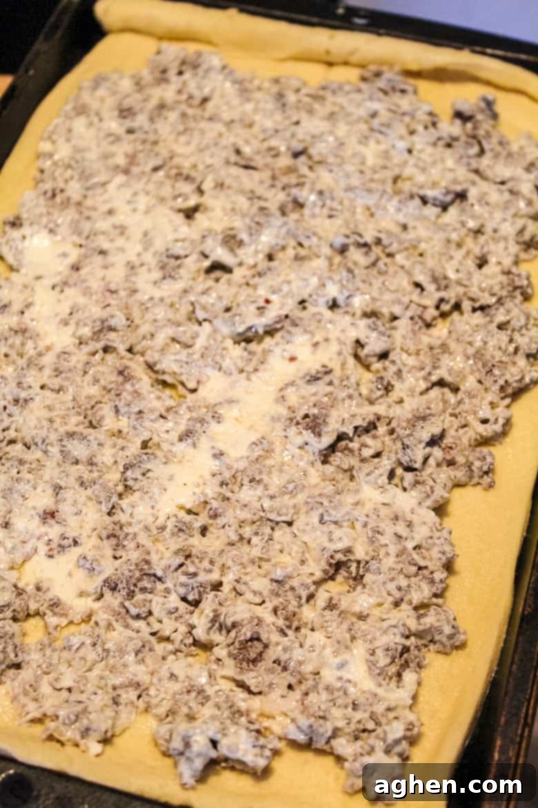 Sausage and cream cheese mixture spread over crescent roll dough on sheet pan