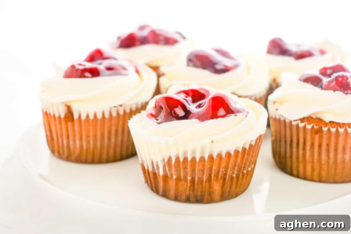 Beautifully frosted vanilla cupcakes, generously topped with vibrant cherry pie filling and fluffy buttercream frosting, arranged artfully.