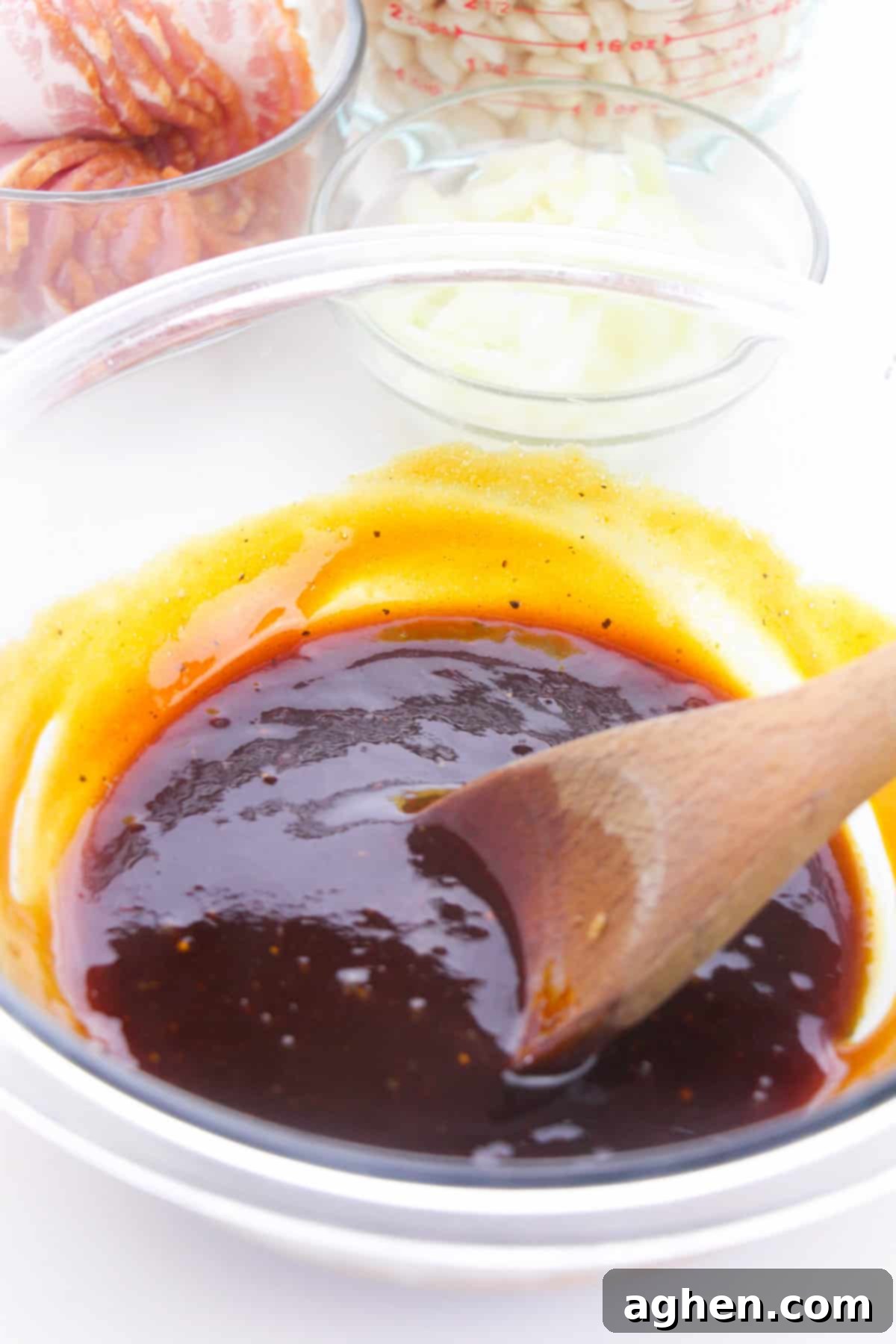 Thick, dark brown sauce in a glass bowl with a wooden spoon.