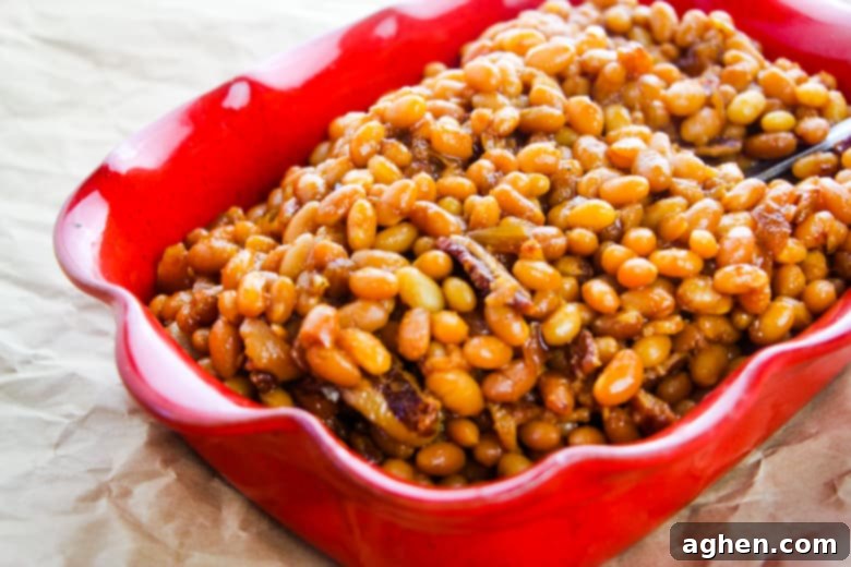 Baked beans with chunks of bacon in red dish.