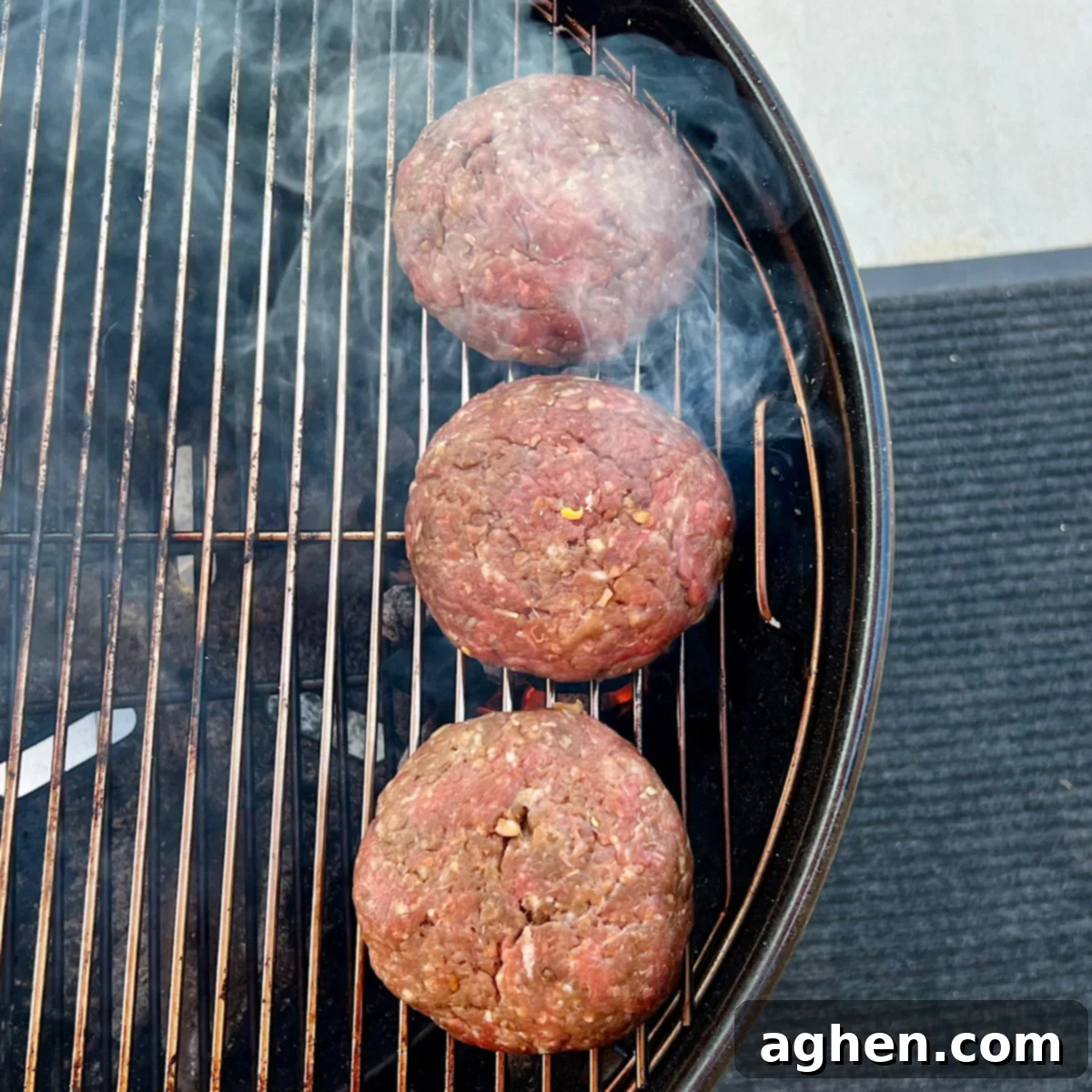 Three Juicy Lucy burgers grilling over direct heat on a Weber Kettle