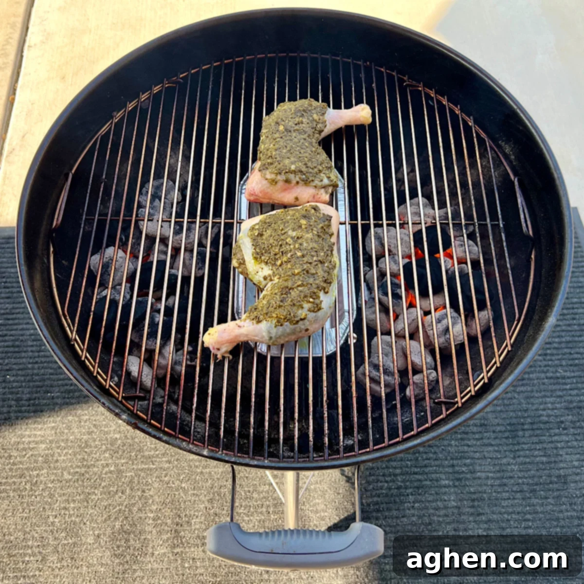 Raw pesto-coated chicken leg quarters placed on the grill grate over indirect heat.