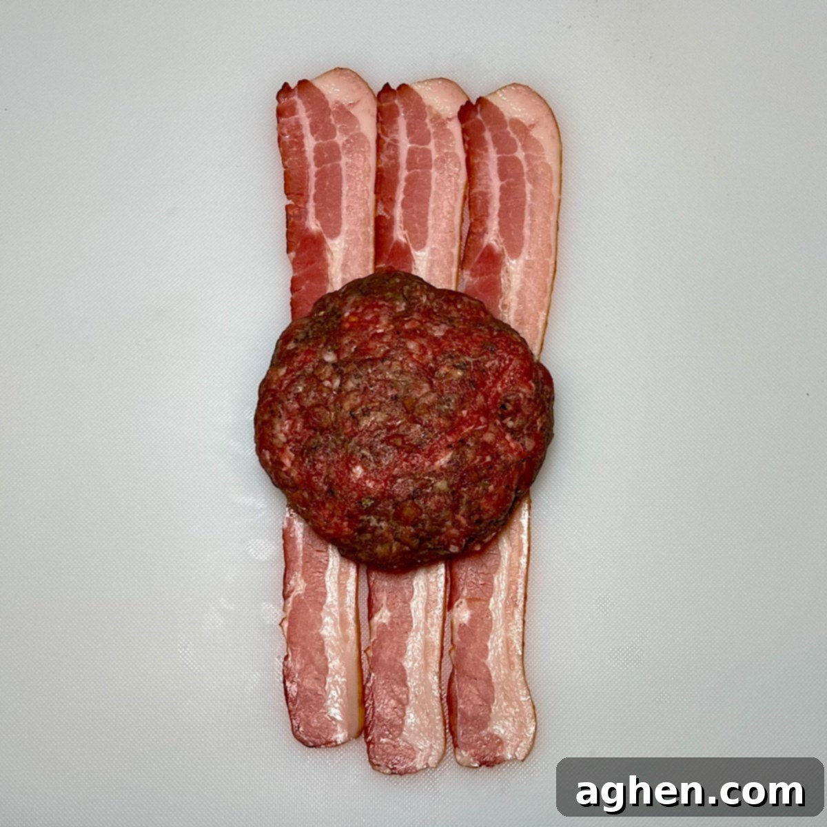 raw burger patty on three strips of bacon, ready for wrapping