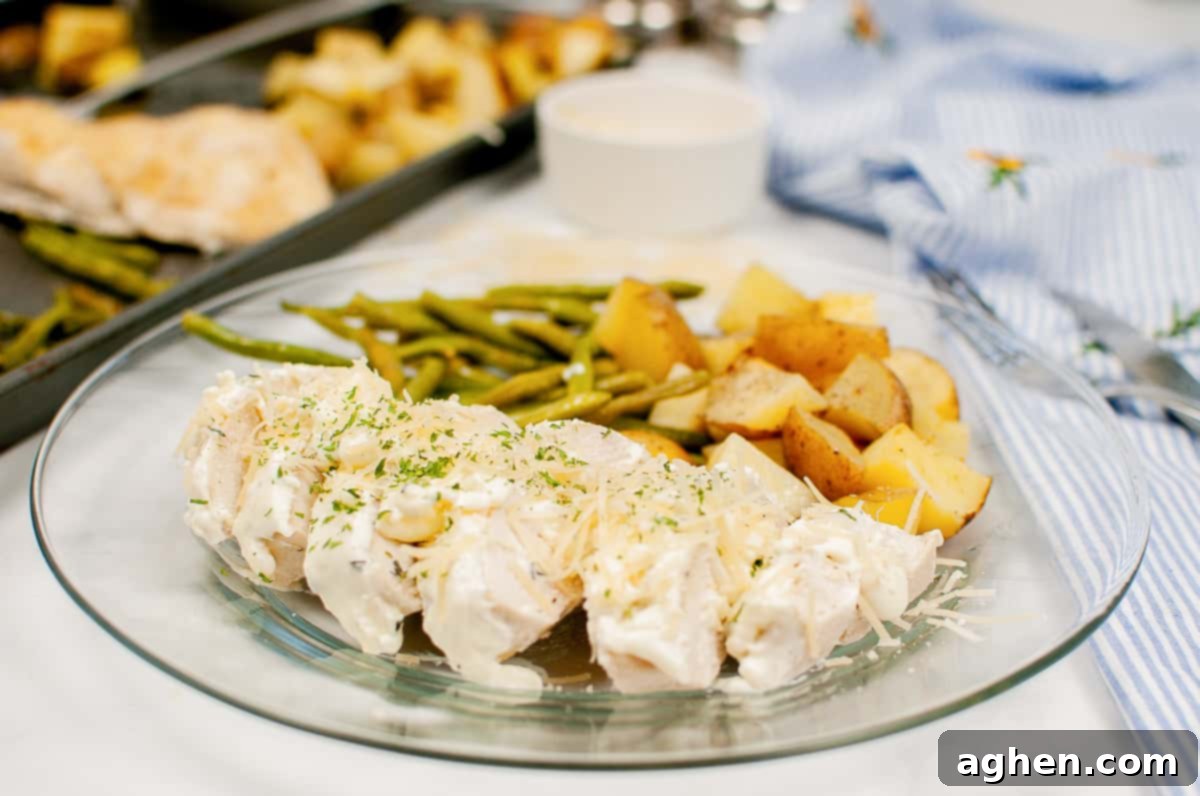 Creamy garlic herb chicken with green beans, and chopped potatoes on a clear plate with sheet pan with additional servings in background