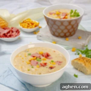 Rich and cream Corn Chowder Soup in a bowl, topped with crispy ham and with bread on the side.