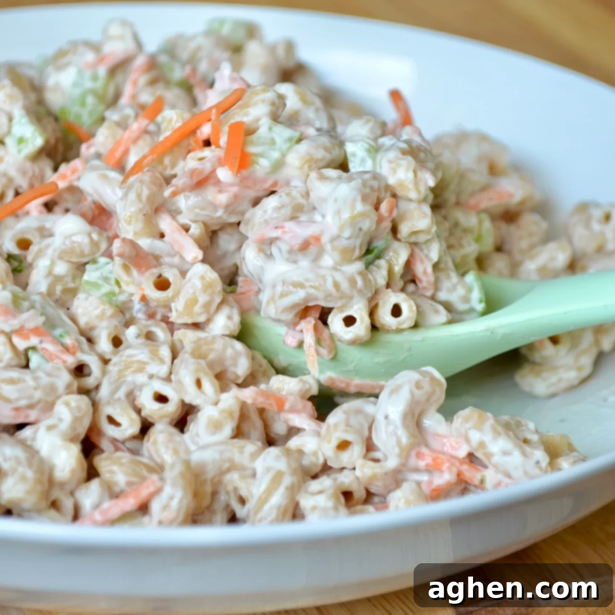 A vibrant bowl of creamy Hawaiian Macaroni Salad, garnished with fresh green onions and shredded carrots.