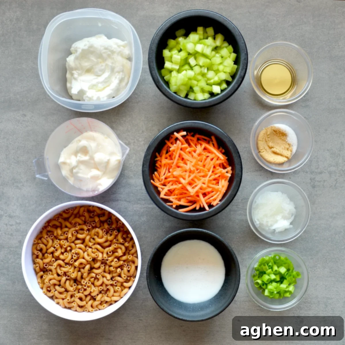 Various ingredients for macaroni salad laid out on a kitchen counter, including pasta, carrots, celery, and dressing components.