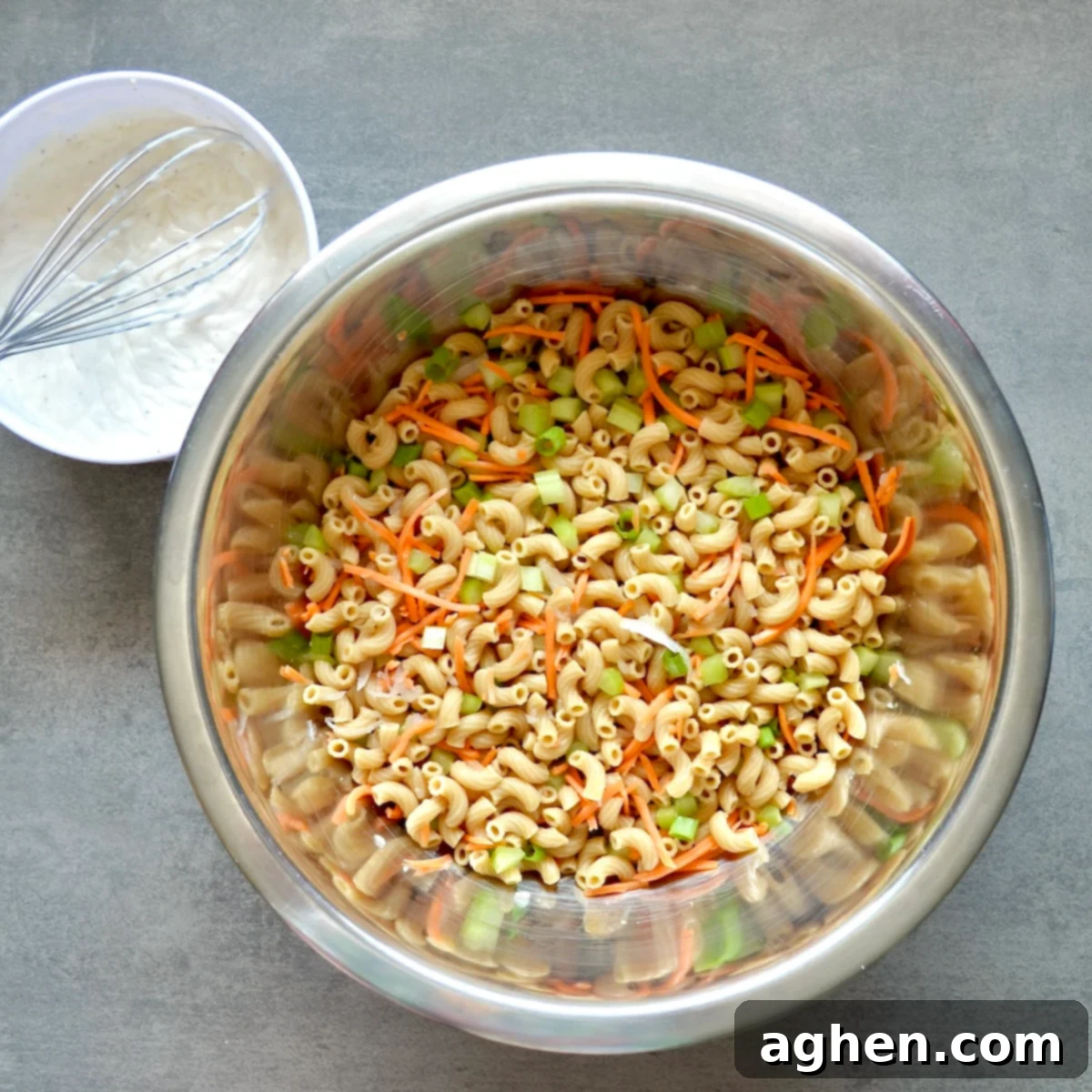 Cooked pasta mixed with chopped vegetables in a large bowl, ready for the dressing.