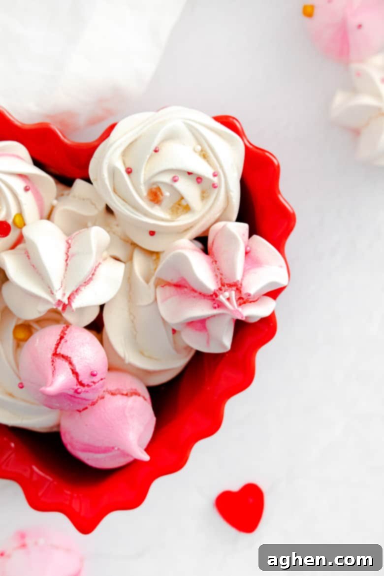 Pink and white Valentine meringue cookies decorated with festive heart sprinkles, presented in a charming red heart-shaped bowl