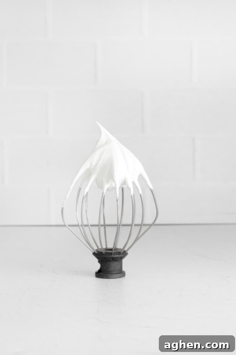 Close-up of a stand mixer whisk attachment showing perfectly formed stiff peaks of fluffy white meringue batter, demonstrating the ideal consistency