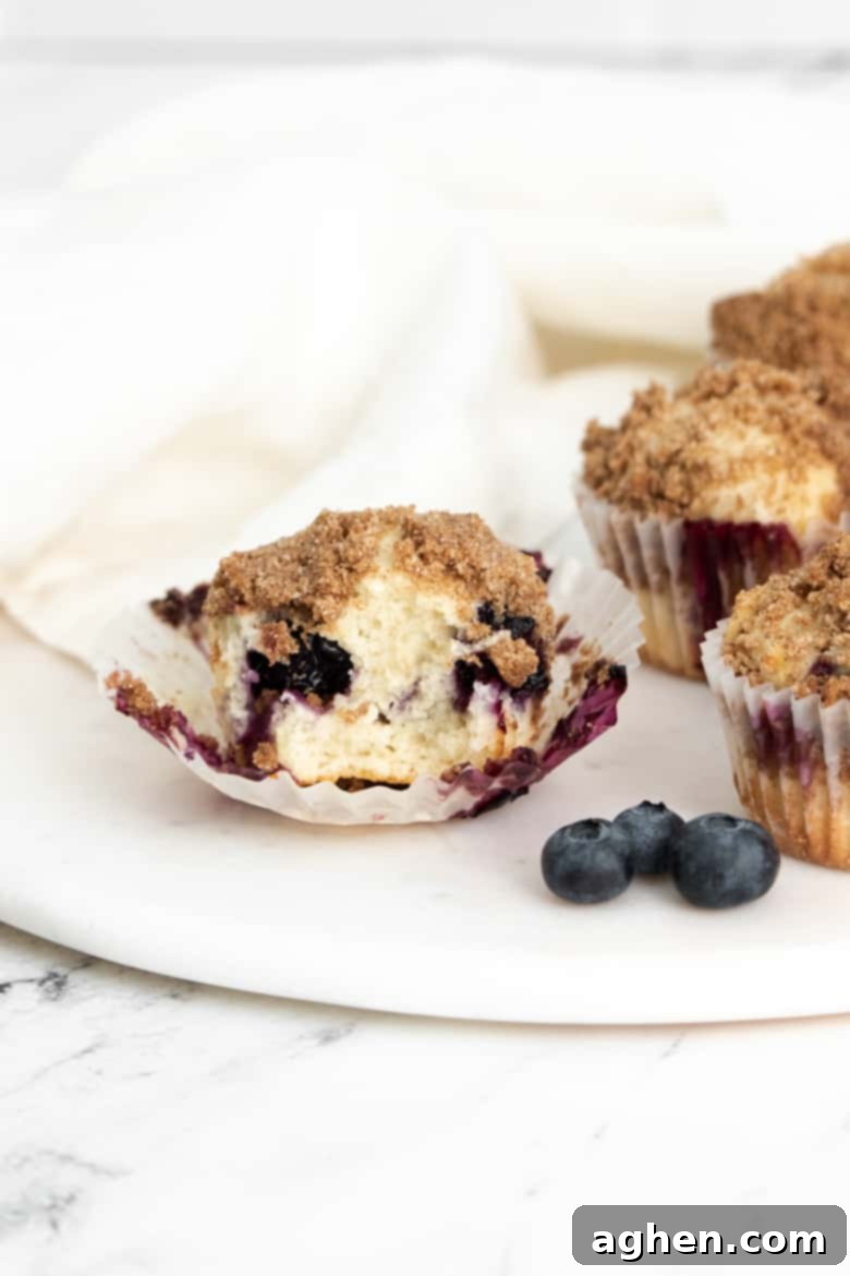 Zesty Lemon Blueberry Crumble Muffins 10 Lemon and Blueberry Muffin with wrapper off and bite taken out of it to show soft and tender crumb.
