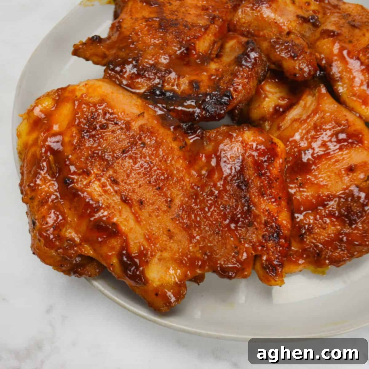 These 15 Recipes Are The Sole Reason My Blackstone Griddle Sees Action In August 3 Close up of a white plate with two bbq chicken thighs. Sauce coats the chicken and the edges are browned and caramelized