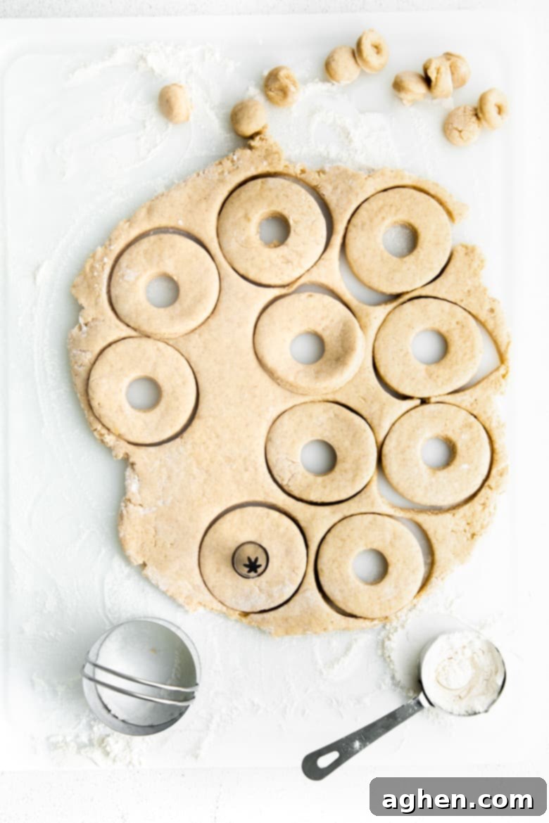 Doughnuts being meticulously cut out of prepared dough using a biscuit cutter for the main shape and a piping tip for the center hole.