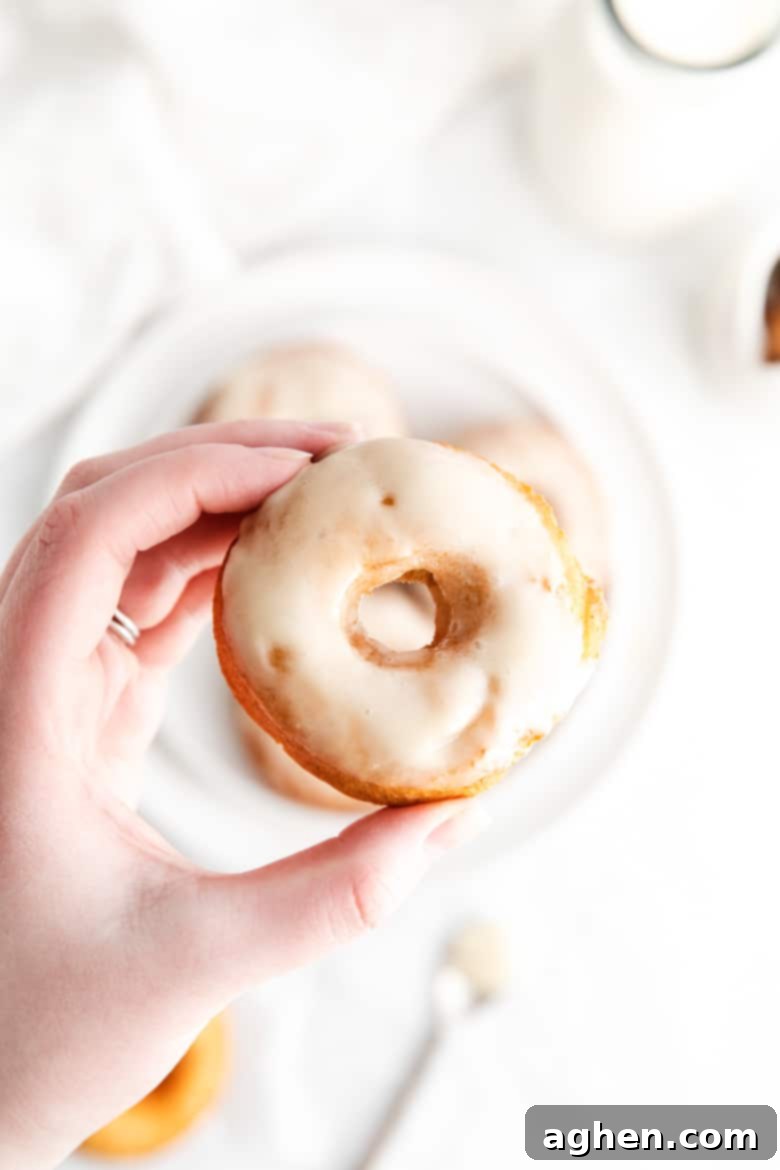 A woman's hand delicately holding a perfectly glazed old-fashioned doughnut, showcasing its craggy texture and tempting finish.