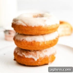 Three beautifully glazed old-fashioned doughnuts stacked on top of one another, set atop a pristine white plate, showcasing their inviting texture and sweet coating.